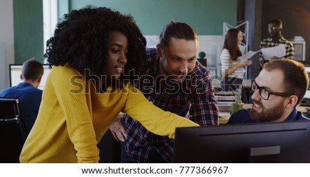 Young succesful team working and discussing a business project at the computer. Multi-ethnic male and female workers in the urban office.