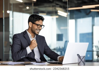 Young successful arab businessman at workplace inside office, man in business suit with laptop celebrating victory received online win notification, boss winner rejoices and celebrates triumph. - Powered by Shutterstock