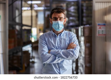 Young successful attractive businessman with surgical mask on standing in warehouse with arms crossed and looking at camera. Corona outbreak concept. - Shutterstock ID 1822756733