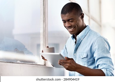 Young Successful Black African Man With Morning Coffee And Tablet Computer Checking On News Of Investments