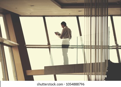 Young Successful Business Man In Penthouse Working On Tbalet,  Modern Bright Duplex Office Apartment Interior  With Staircase And Big Windows