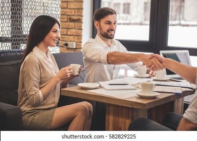 Young successful business people are drinking coffee, discussing affairs and smiling while working in cafe. Men are shaking hands