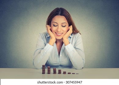 Young Successful Business Woman Sitting At Table Looking At Growing Stack Of Coins. Financial Freedom Target Success Concept  