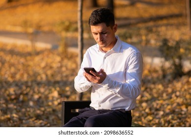 Young And Successful Businessman Standing In Park And Reading A Message On His Smartphone. Buisness Portrait.