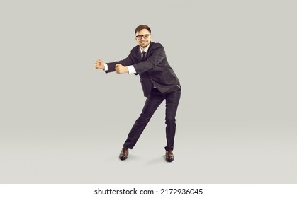 Young Successful Caucasian Business Man Smiles And Performs Victory Dance After Conclusion Of Lucrative Contract Or Sale Of Company Is Dressed In Formal Suit, Stands On Studio Background