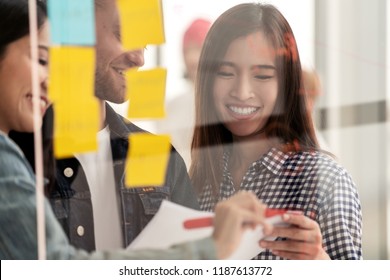 Young successful creative woman and team smile and brainstorm on project at office concentrate on paper, yellow post note and sticky note. Close up view of group sharing idea on glass wall concept. - Shutterstock ID 1187613772