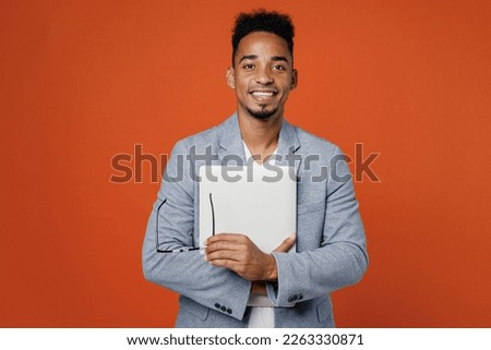 Young successful employee IT business man corporate lawyer wearing classic formal grey suit shirt work in office hold closed laptop pc computer glasses isolated on plain red orange background studio