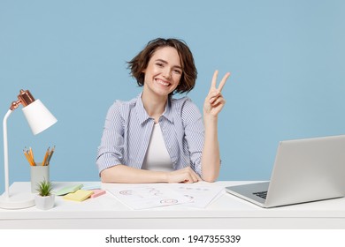 Young successful employee business woman in casual shirt sit work at white office desk with pc laptop show victory v-sign gesture isolated on pastel blue background studio portrait Achievement concept
