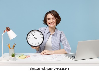Young successful employee business woman 20s in casual shirt sit work at white office desk with pc laptop hold in hands clock isolated on pastel blue background studio portrait Time management concept