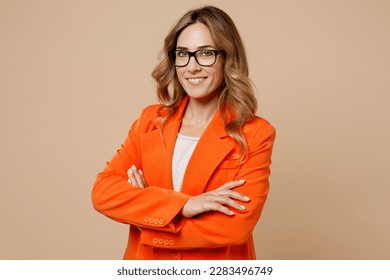 Young successful employee business woman corporate lawyer wear classic formal orange suit glasses work in office look camera hold hands crossed folded isolated on plain beige color background studio