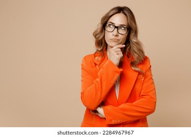 Young successful employee business woman corporate lawyer 30s wears classic formal orange suit glasses work in office prop up chin look aside on area isolated on plain beige color background studio - Powered by Shutterstock