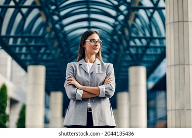 A young, successful female boss dressed smart casual is standing at the business center with arms crossed and looking for a new opportunity. - Shutterstock ID 2044135436