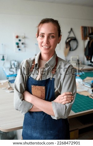 Young successful female leather worker in apron looking at camera