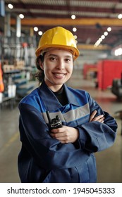 Young successful female worker of modern industrial plant in workwear and protective helmet standing in front of camera in large workshop