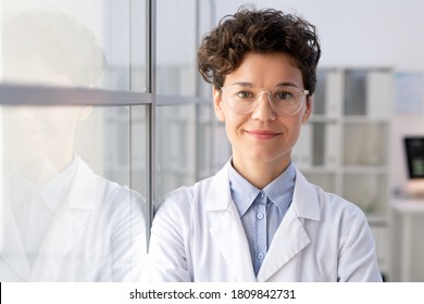 Young successful female worker of scientific laboratory in whitecoat and eyeglasses standing by glass wall inside office in front of camera - Shutterstock ID 1809842731