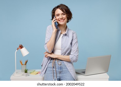 Young Successful Fun Secretary Employee Business Woman In Casual Shirt Work Stand At White Office Desk With Pc Laptop Talking Speaking By Mobile Cell Phone Isolated On Pastel Blue Background Studio