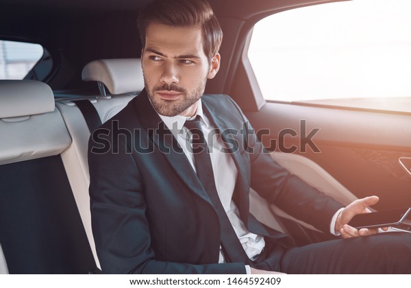 Young and successful. Handsome young\
man in full suit looking away while sitting in the\
car