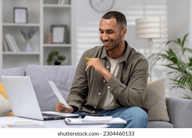 Young successful hispanic man at home sitting on sofa in living room, calculating and paying bills, man with calculator and laptop online paying for rent and loan. - Powered by Shutterstock