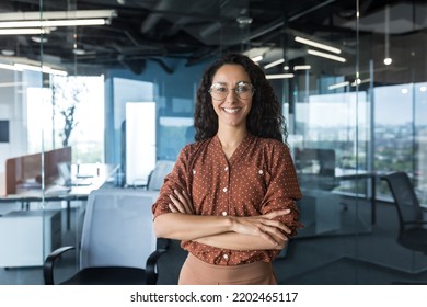 Young successful Indian IT developer female engineer working inside the office of a development company portrait of a female programmer with curly hair and glasses, smiling and looking at the camera.