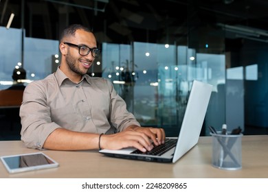 Young successful Indian programmer working inside modern development company, man using laptop to write code for software.