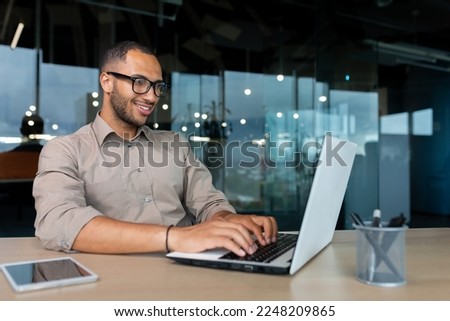 Young successful Indian programmer working inside modern development company, man using laptop to write code for software.