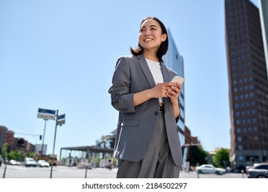 Young successful smiling pretty Asian business woman, korean professional businesswoman holding cellphone using phone standing on big city urban street. Mobile apps technology. - Powered by Shutterstock