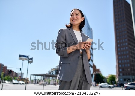 Young successful smiling pretty Asian business woman, korean professional businesswoman holding cellphone using phone standing on big city urban street. Mobile apps technology.
