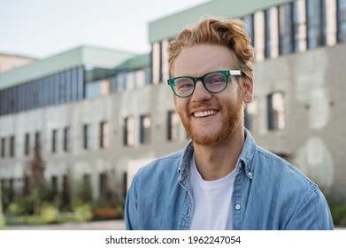 Young successful student looking at camera standing in university campus, education concept. Portrait of handsome smiling Irish man wearing stylish eyeglasses posing for pictures outdoors 	 - Shutterstock ID 1962247054