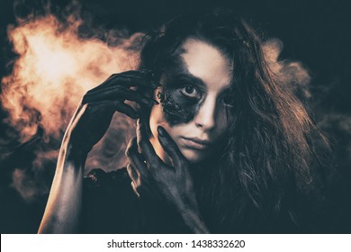 a young succubus girl on a smoke background with hands stained with soot and a burned face with an expressive look and a pleasant appearance in a black dress