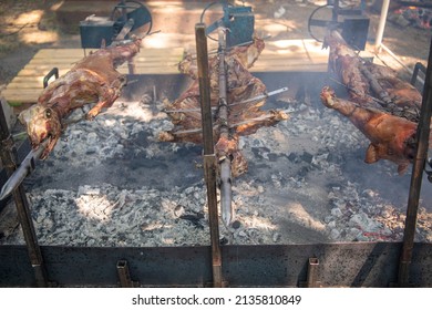 A young suckling lamb (sheep) and pig on skewer. Whole roasted pig and lamb on a rotating steel spit with fire and smoke. Traditional grill of Serbia, in Balkans, countryside.