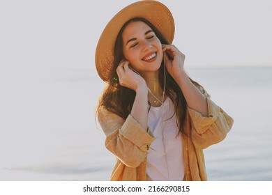 Young sunlit cute excited traveler tourist woman 20s wearing straw hat shirt summer casual clothes earphones listen to music outdoors on sea beach background People vacation lifestyle journey concept. - Powered by Shutterstock