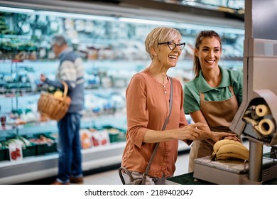 Young Supermarket Worker Assisting Senior Woman In Measuring Fruit On Grocery Scale.