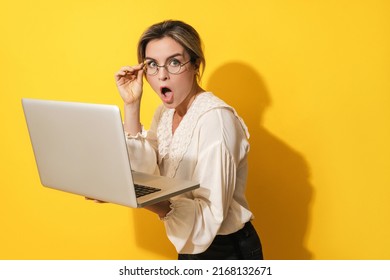 Young Suprised Woman Wearing Eyeglasses Using Laptop Computer On Yellow Background