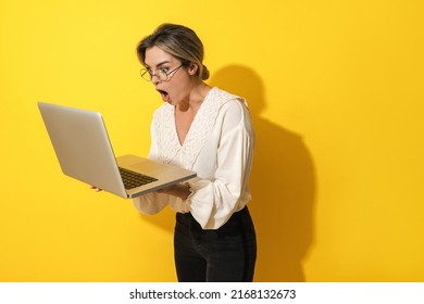 Young Suprised Woman Wearing Eyeglasses Using Laptop Computer On Yellow Background