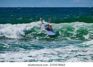 A young surfer is catching a wave while lying on a surfboard in the ocean under a clear blue sky learning to surf