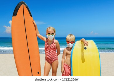 Young surfer kids with surf boards wear protective mask on sea beach. Cancelled cruises, tours due coronavirus COVID-19 epidemic. Travel ban for family vacation, tourism industry crisis at summer 2020