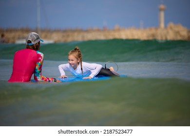 Young Surfer Learn To Ride On Surfboard With Instructor At Surfing School. Active Family Lifestyle, Kids Water Sport Lessons, Swimming Activity In Summer Camp. Vacation With Child.