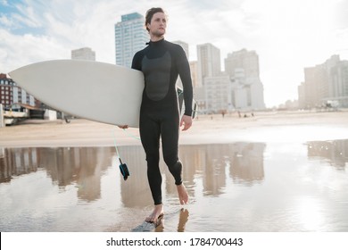 Young surfer standing in the ocean with his surfboard in a black surfing suit. Sport and water sport concept. - Powered by Shutterstock