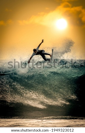 Young surfer with with wetsuit enjoying big waves in Tenerife, Canary Islands. Sporty boy riding his surf board on the ocean wave. Brave teenager making tricks on the rough sea during a competition.