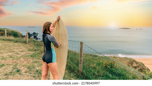 Young Surfer Woman With Wetsuit Posing With Surfboard Looking At The Beach From The Shore