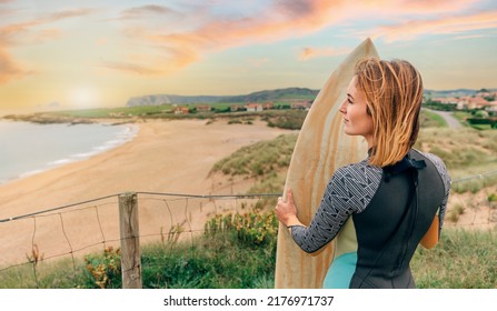 Young Surfer Woman With Wetsuit And Surfboard Looking At The Beach From The Shore