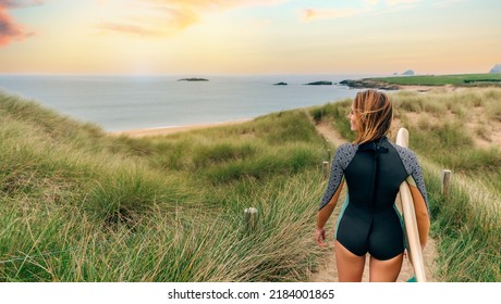 Young Surfer Woman With Wetsuit And Surfboard Going To The Beach Through The Dunes