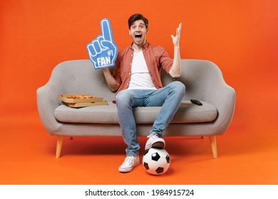 Young surprise man football fan in shirt support team with soccer ball sit on home sofa watch tv live stream hold pizza foam glove finger spread hand isolated on orange background People sport concept - Powered by Shutterstock