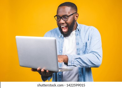 Young Surprised African American Man Standing And Using Laptop Computer Isolated Over Yellow Background.