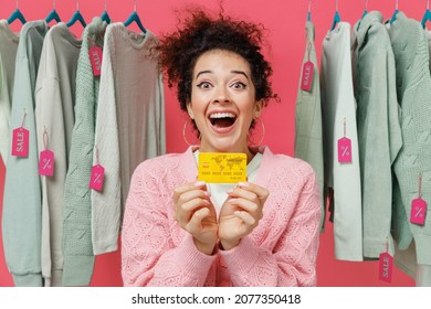 Young Surprised Amazed Happy Female Costumer Woman Wear Sweater Stand Near Clothes Rack With Tag Sale In Store Showroom Hold In Hand Credit Bank Card Isolated On Plain Pink Background Studio Portrait