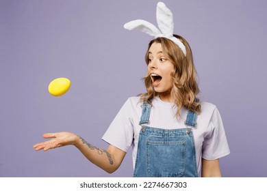 Young surprised cheerful fun woman wear casual clothes bunny rabbit ears toss up colorful yellow egg isolated on plain pastel light purple background studio portrait. Lifestyle Happy Easter concept - Shutterstock ID 2274667303