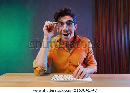 Young surprised copywriter geek software engineer IT specialist programmer man in yellow shirt touch glasses work at office writing code type script on keyboard look camera Program development concept