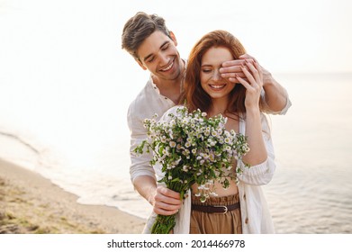 Young surprised couple family man woman in white clothes rest relax together boyfriend meet girlfriend close eyes gift give bouquet flowers at sunrise over sea sand beach outdoor seaside in summer day
