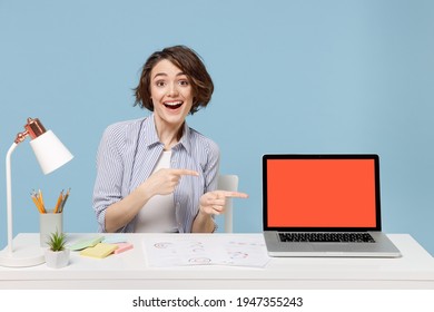 Young surprised employee business woman in casual shirt sit work at white office desk point finger on pc laptop computer blank screen workspace area isolated on pastel blue background studio portrait