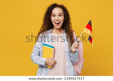 Young surprised excited cool black teen girl student she wearing casual clothes backpack bag hold books Germany flag isolated on plain yellow color background. High school university college concept